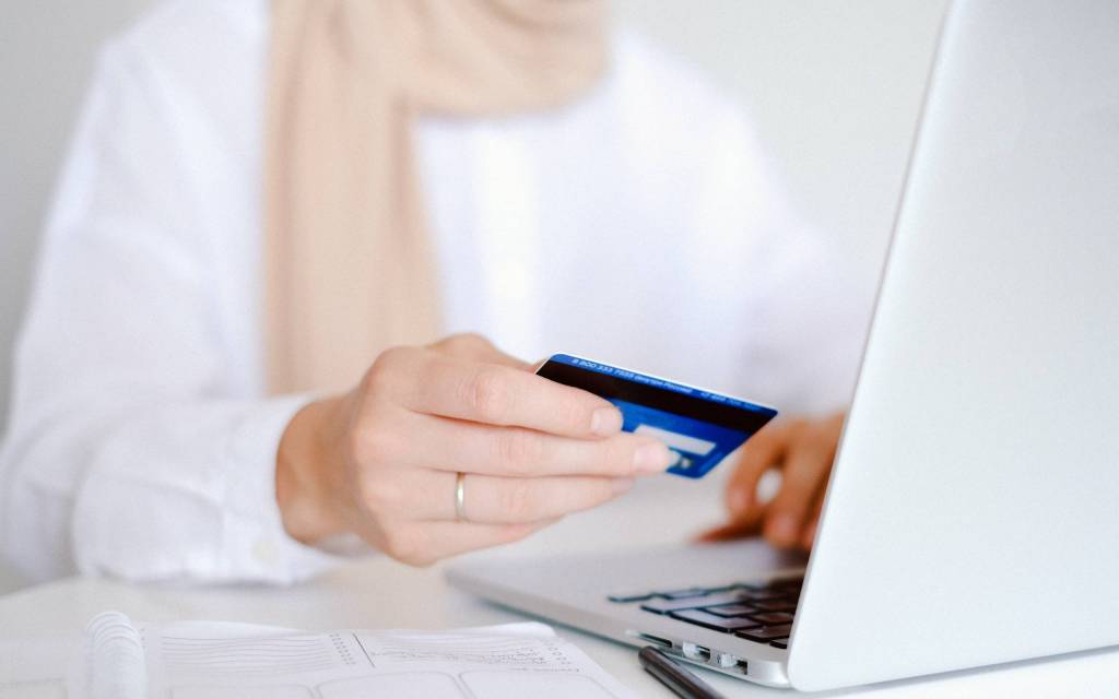 Persona con una tarjeta de crédito en la mano y otra en una laptop realizando una transacción de la industria financiera