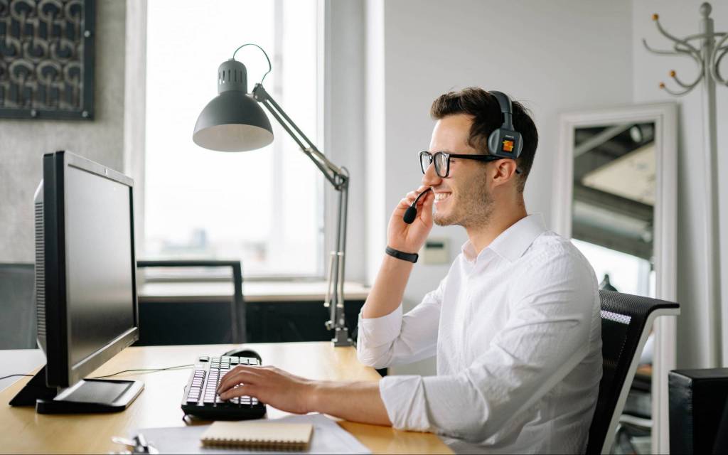 Hombre frente a una computadora conversa a través de un headphone en un proceso de gestión de experiencia del cliente.
