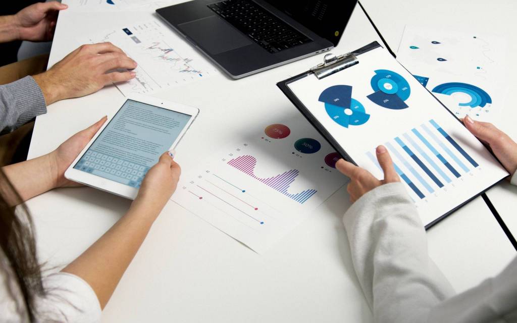 Personas trabajando en una mesa con dispositivos y papeles impresos con tendencias tecnológicas.
