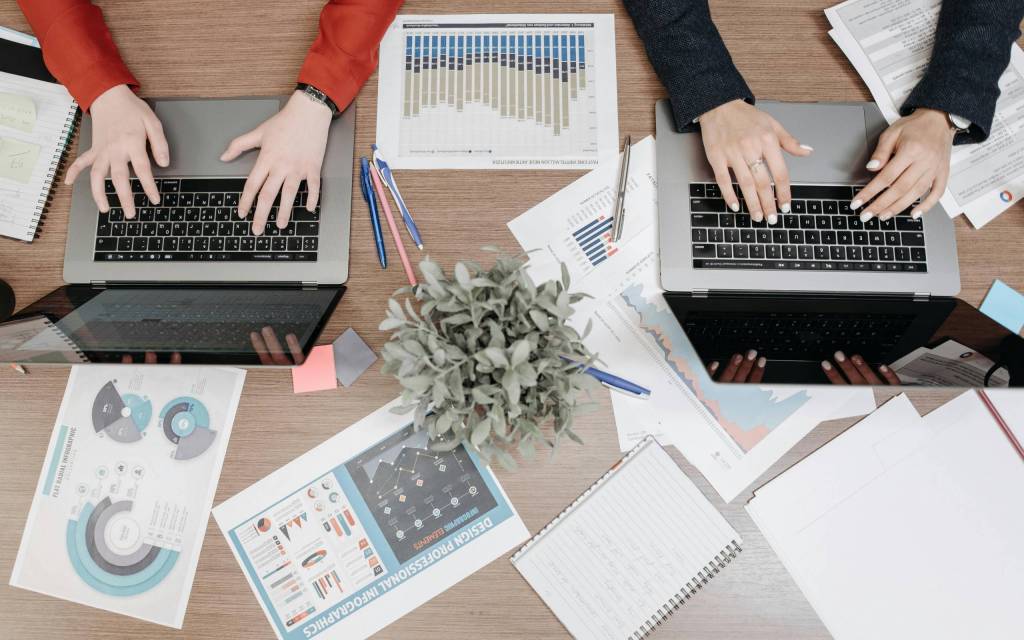 Manos de dos personas trabajando en computadoras con informacion no estructurada